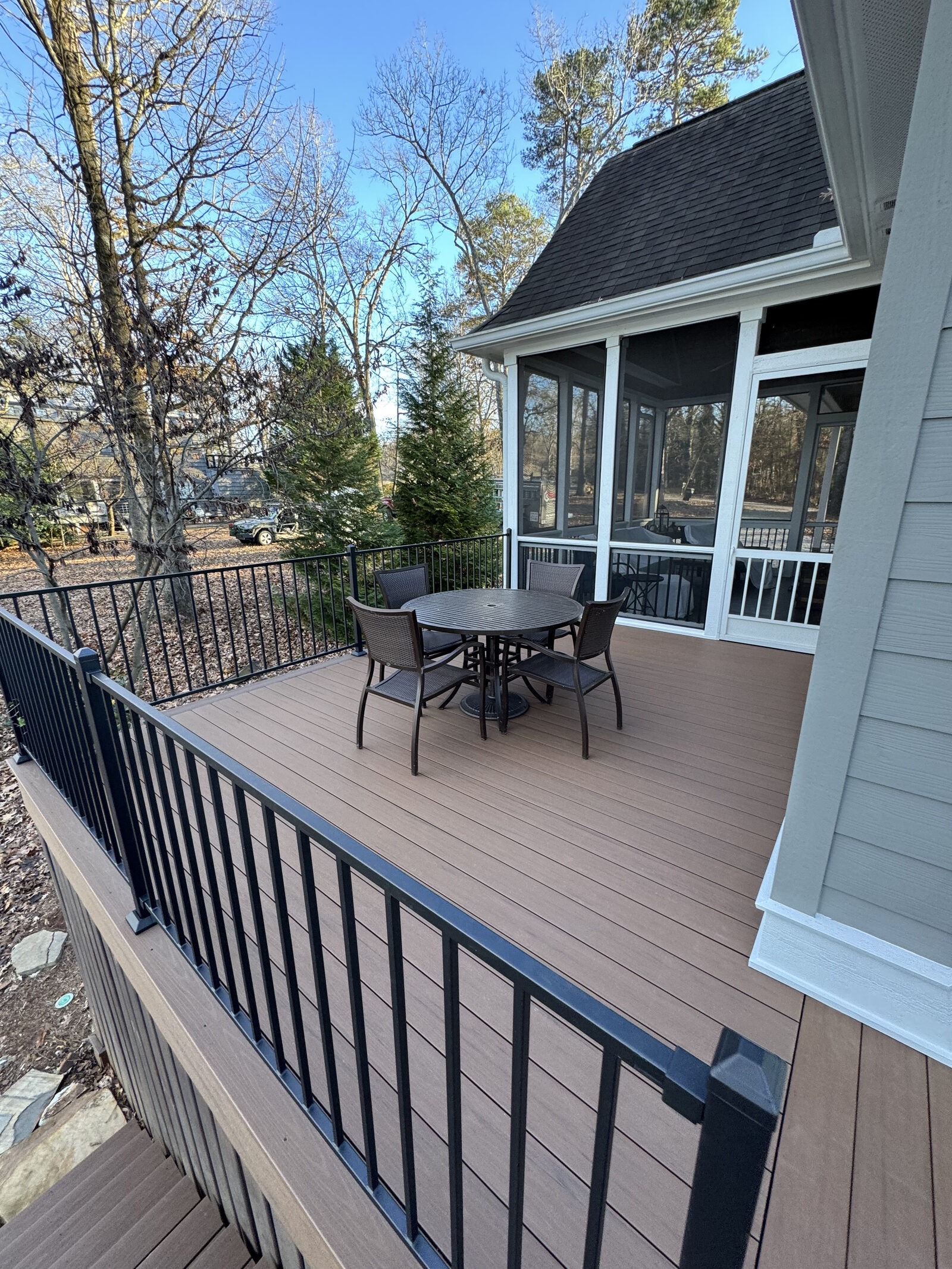 A black metal patio table and four chairs sits on a newly built deck in front of a screened-in porch.
