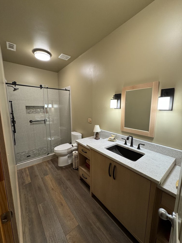 A completed bathroom remodel with tile shower, glass doors, vanity, mirror, and lighting.